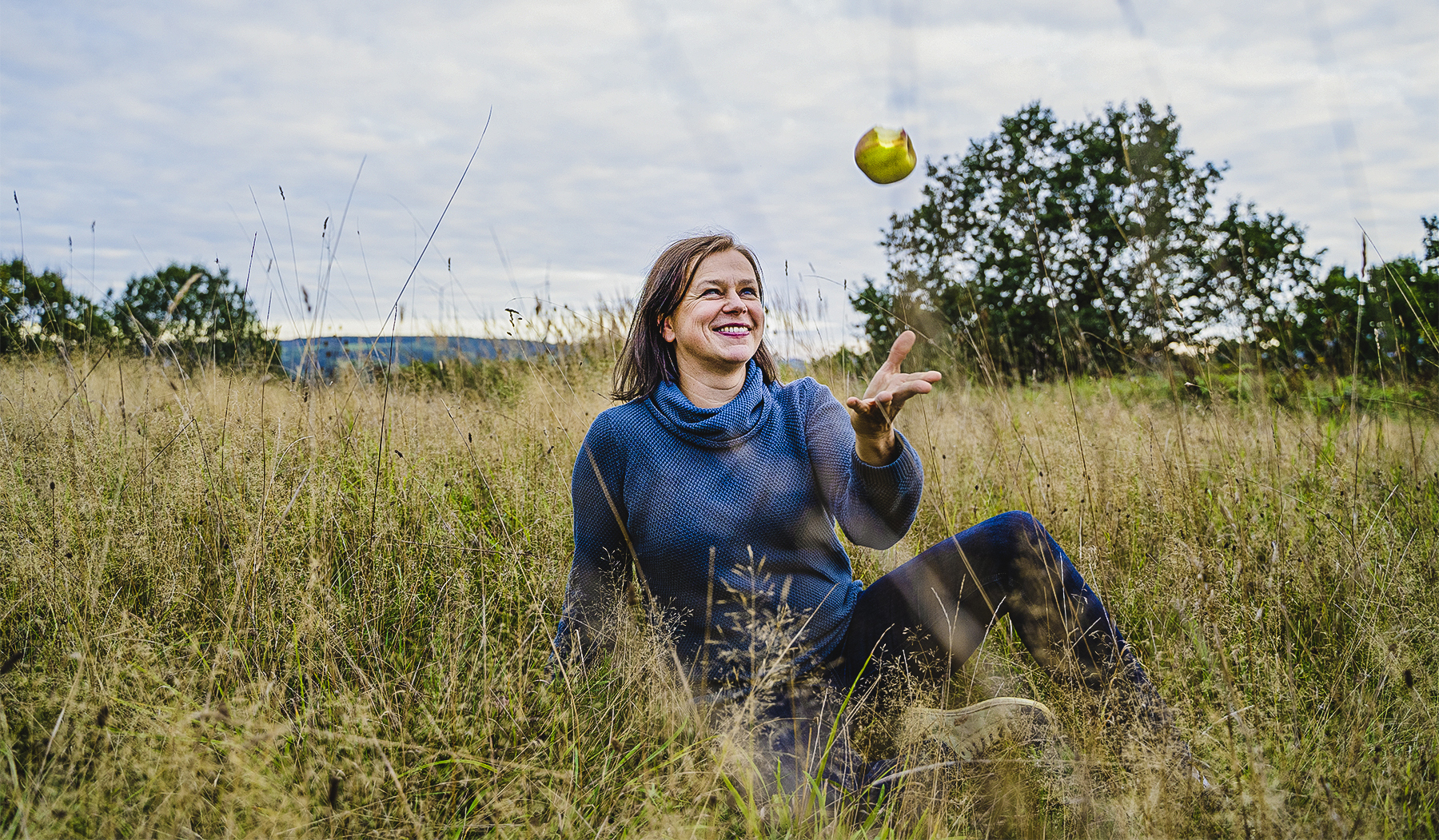 Tanja Busse liegt auf einer Wiese und wirft einen Apfel in die Luft