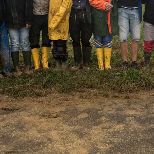 Viele Menschen stehen nebeneinander auf dem Feld. Im Fokus des Bildes sind ihre Gummistiefel