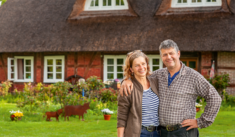 Paar vor einem Bauernhaus mit Reetdach