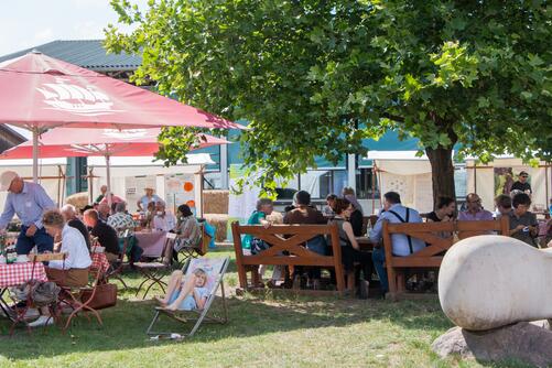 Besucher:innen sitzen an Tischen im Freien 