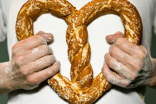 Bäcker hält eine Brezel in Herzform vor der Brust