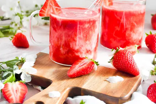 Erdbeer-Kefir-Mocktail in Glastassen mit Glasstrohalm angerichtet auf einem Brett mit Erdbeeren